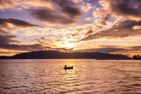 Sea fishing, Fisherman in a boat, Fishing during sunset, Active rest. A fisherman casts a fishing rod into the water while standing in a boat during sunset.の写真素材