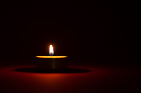 One candle burning in the dark, black and red backgroundの写真素材