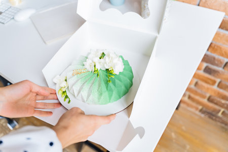 Hands of an unrecognizable female confectioner packing a mousse cake in a gift box and tying it with a ribbon, close-upの写真素材