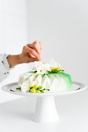 A woman's hand fixes a white flower on a chic mousse cake standing on a stylish tray