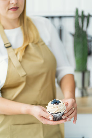 The blonde confectioner holds in her hands a black stand on which there are chocolate muffins with white cream and berries. close-upの写真素材