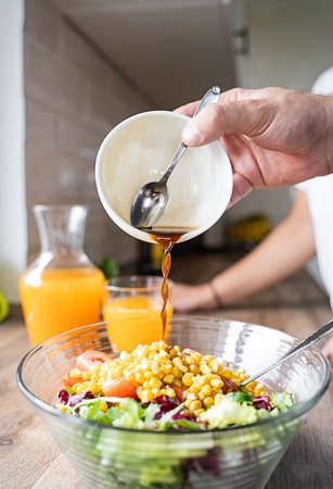 A man puts sauce on a salad. He is preparing food for breakfastの写真素材