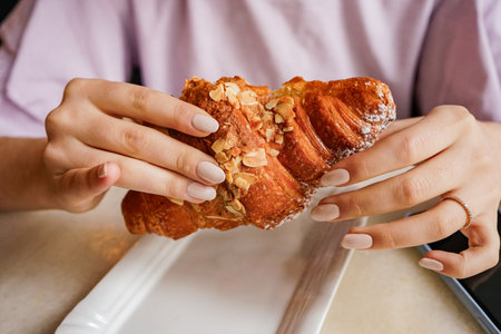 Close-up of a girls hands holding a delicious croissant. The concept of a snack in a cafeの写真素材