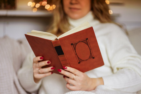 A girl sits in warm white clothes at home in winter and reads a bookの写真素材