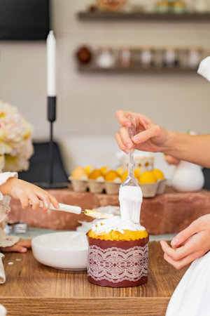 Mom and child together smear cream on Easter cake with brushes. High quality photo