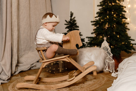 A little boy rides a wooden rocking horse near the Christmas tree. A gift for the Christmas treeの写真素材