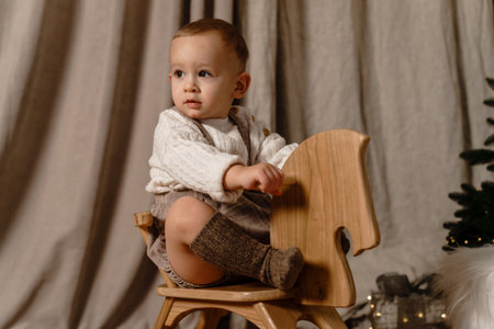 Little boy in casual overalls and socks rides a rocking horse near a Christmas treeの写真素材