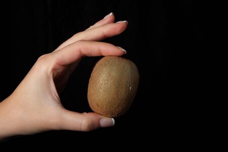 Kiwi in a woman hand on black backgroundの写真素材