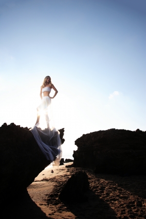 Beautiful young woman on the beach wrapped in white wedding veil at sunriseの写真素材