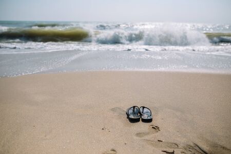 Flip flops on a sandy beach in Summer vacation with waving sea.