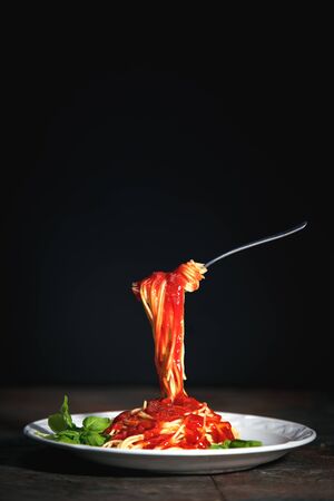 Tasty appetizing classic italian spaghetti pasta with tomato sauce, cheese parmesan and basil on plate on dark tableの写真素材