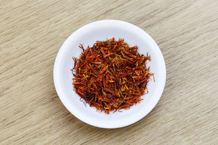 Dry red saffron in white bowl on wooden tableの写真素材