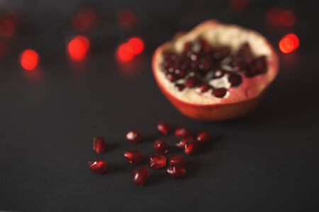 ripe beautiful cut pomegranate on a black background with red lanterns. pomegranate seeds are scattered nearby.の写真素材