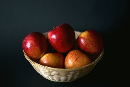 Wicker basket with red apples on a black background. Farm fresh natural products. Healthy food,...