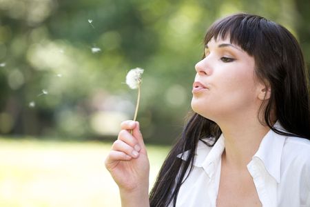 attractive woman bloweing dandelion at meadow