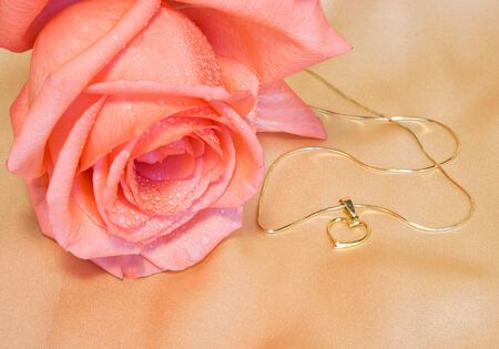 Golden chain with a heart and pink rose on silk backgroundの写真素材