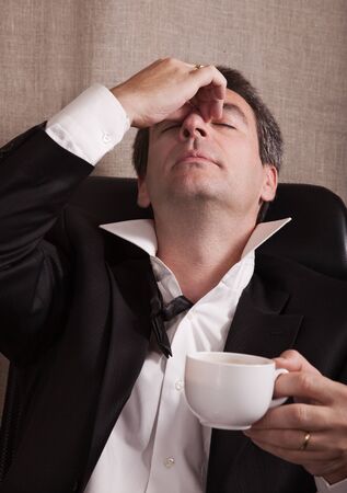 Tired dressed-up man after end of a party with a cup of coffeeの写真素材