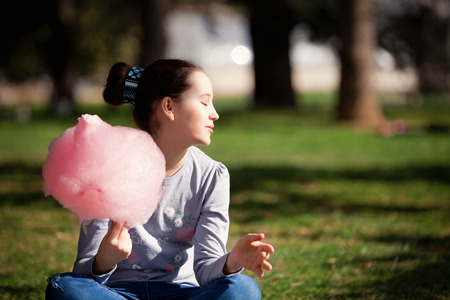 Young girl eating cotton candy in the parkの写真素材
