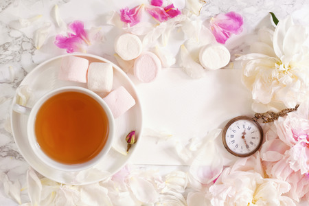 Tea time. Flat lay over light background with peonies, marshmalows and cup of teaの写真素材