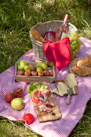 Picnic at the park on the grass: tablecloth, basket, healthy food, rose wine and accessoriesの写真素材