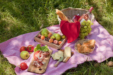 Picnic at the park on the grass: tablecloth, basket, healthy food, rose wine and accessoriesの写真素材