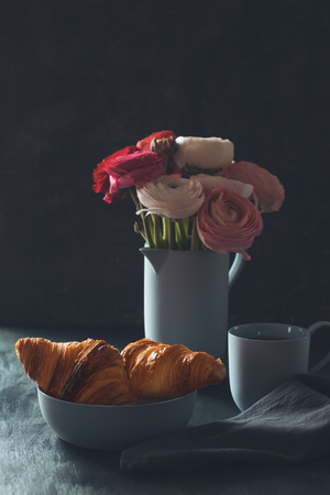 Romantic breakfast ith coffee, croissants and beautiful bouquet of flowers. Dark photoの写真素材