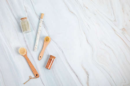Natural bristle brushes, bath salt and clay masks in glass jars on white marble background. Spa, self care and wellness concept. Flat lay, top viewの写真素材