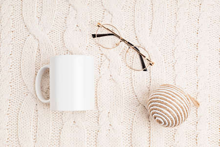 Mockup with white mug and glasses on white woolen knitted background. Cozy reading concept. Flat...