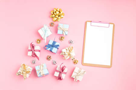 Christmas ornamets and gift boxes laid out in shape of Christmas tree and clipboard on pink background. Winter holidays gift list mockup with copy space. Flat lay, overhead viewの写真素材