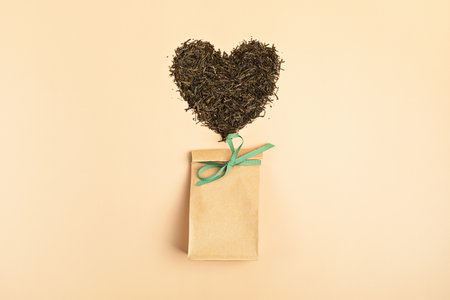 Craft package back with dry green tea leaves in heart shape on beige background. Eco friendly organic brand concept. Branding mockup. Flat layの写真素材