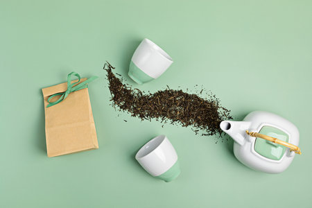 White ceramic tea pot with dry green tea leaves and paper bag on pastel background. Eco friendly organic brand concept. Branding mockupの写真素材