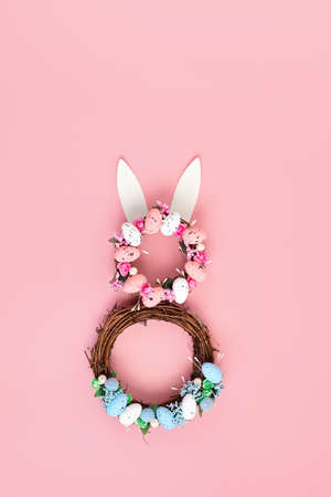 Easter bunny made of wreath of eggs and flowers over pink pastel backgroundの写真素材