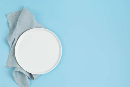 Empty white plate and cotton napkin on blue backdrop. Food background for menu, recipe book