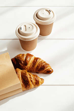 Hot coffee on the go and croissants for breakfast. Biodegradable, disposable takeaway cupsの写真素材