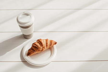 Hot coffee on the go and croissants for breakfast. Biodegradable, reusable takeaway cupの写真素材