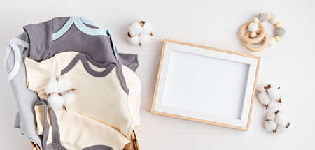 Gender neutral baby garment and accessories and empty frame mockup. Organic cotton clothes, newborn fashion, branding, small business idea. Flat lay, top viewの写真素材