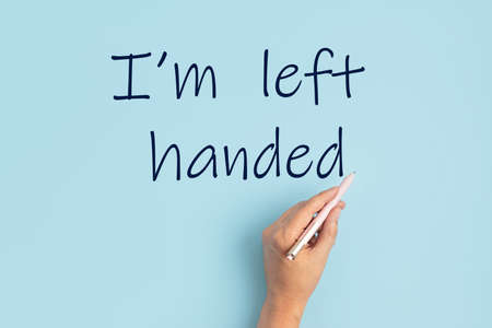 Text I am left handed and left hand with pen over blue background. International left handers day...