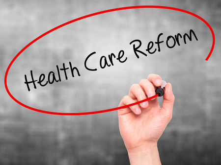 Man Hand writing Health Care Reform with black marker on visual screen. Isolated on grey. Business, technology, internet concept.の写真素材