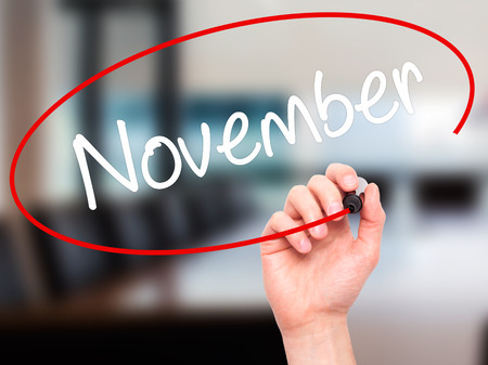 Man Hand writing November with black marker on visual screen. Isolated on background. Business, technology, internet concept. Stock Photoの写真素材