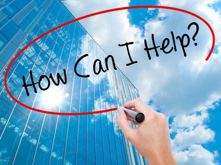 Man Hand writing How Can I Help? with black marker on visual screen. Business, technology, internet concept. Modern business skyscrapers background. Stock Photoの写真素材