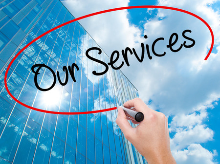 Man Hand writing Our Services with black marker on visual screen. Business, technology, internet concept. Modern business skyscrapers background. Stock Photoの写真素材