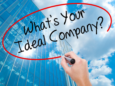 Man Hand writing Whats Your Ideal Company? with black marker on visual screen.  Business, technology, internet concept. Modern business skyscrapers background. Stock Photoの写真素材