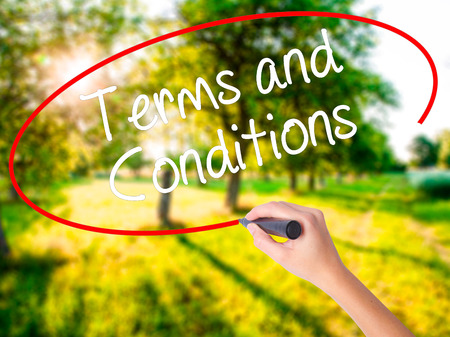 Woman Hand Writing Terms and Conditions on blank transparent board with a marker isolated over green field background. Business concept. Stock Photoの写真素材