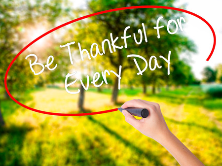 Woman Hand Writing Be Thankful for Every Day   on blank transparent board with a marker isolated over green field background. Business concept. Stock Photoの写真素材