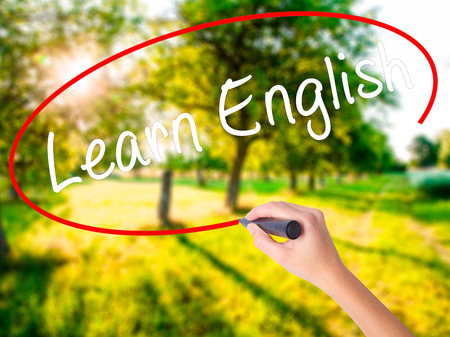 Woman Hand Writing Learn English on blank transparent board with a marker isolated over green field background. Business concept. Stock Photoの写真素材