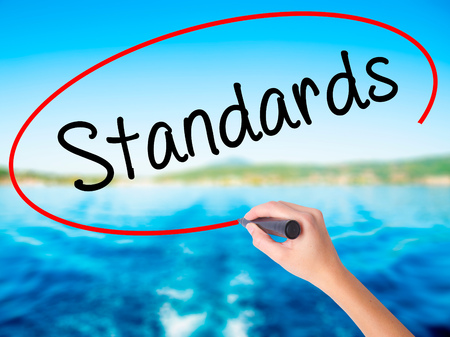 Woman Hand Writing Standards on blank transparent board with a marker isolated over water background. Business concept. Stock Photoの写真素材