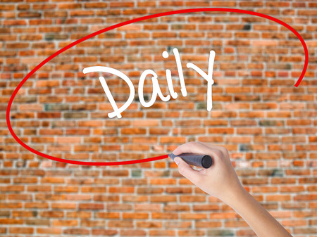 Woman Hand Writing Daily with black marker on visual screen. Isolated on bricks. Business concept. Stock Photoの写真素材