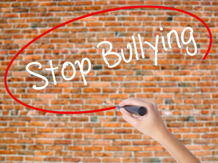 Woman Hand Writing Stop Bullying with black marker on visual screen. Isolated on bricks. Business concept. Stock Photoの写真素材