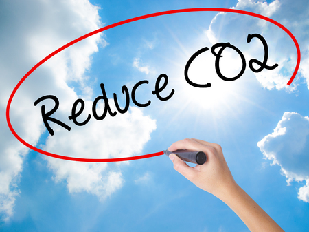 Woman Hand Writing Reduce CO2 with black marker on visual screen. Isolated on Sunny Sky. Business concept. Stock Photoの写真素材