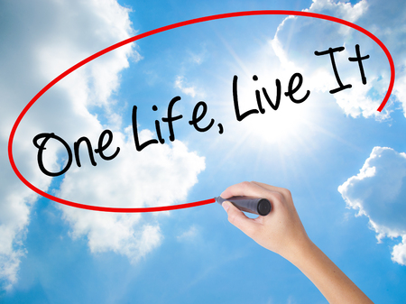 Woman Hand Writing One Life Live It with black marker on visual screen. Isolated on Sunny Sky. Business concept. Stock Photoの写真素材
